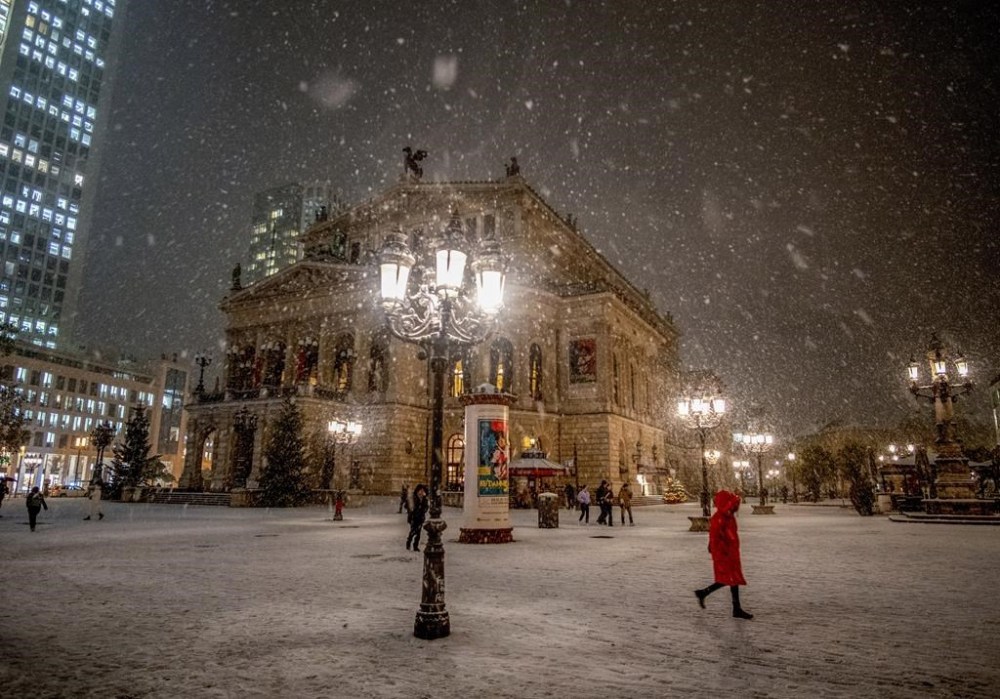 Snow falls as people stand in front of the Old Opera in Frankfurt, Germany, Monday, Dec. 4, 2023. (AP Photo/Michael Probst)