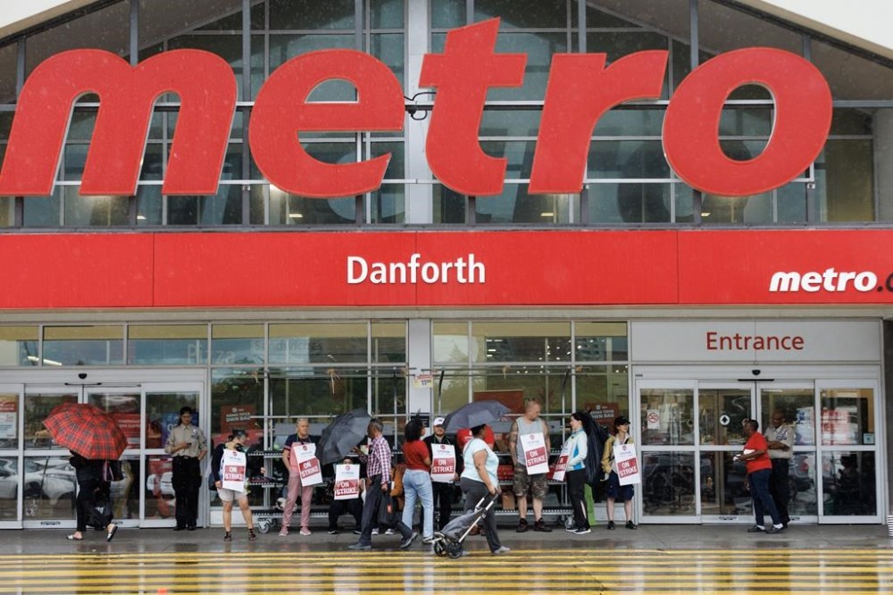 More than a month after 3,700 grocery store workers walked off their jobs at Toronto-area Metro stores in July, they returned to work under a new contract that Unifor called 'historic.' Customers, workers, and security stand outside a Metro grocery store in Toronto on July 29.THE CANADIAN PRESS/Cole Burston