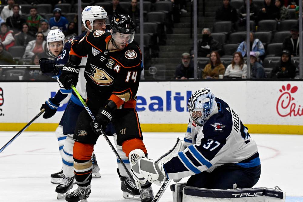 Winnipeg Jets goaltender Connor Hellebuyck, right, catches the puck in front of Anaheim Ducks center Adam Henrique (14) during the second period. (Alex Gallardo / The Associated Press)
