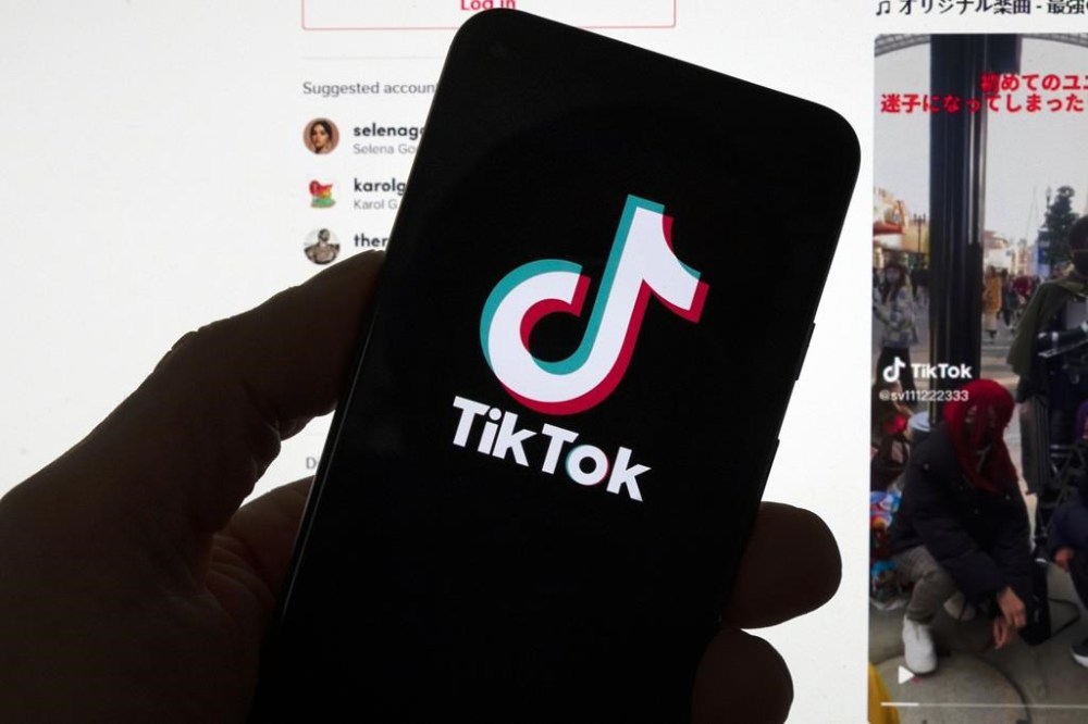 The TikTok logo is seen on a mobile phone in front of a computer screen which displays the TikTok home screen, March 18, 2023, in Boston. THE CANADIAN PRESS/AP-Michael Dwyer