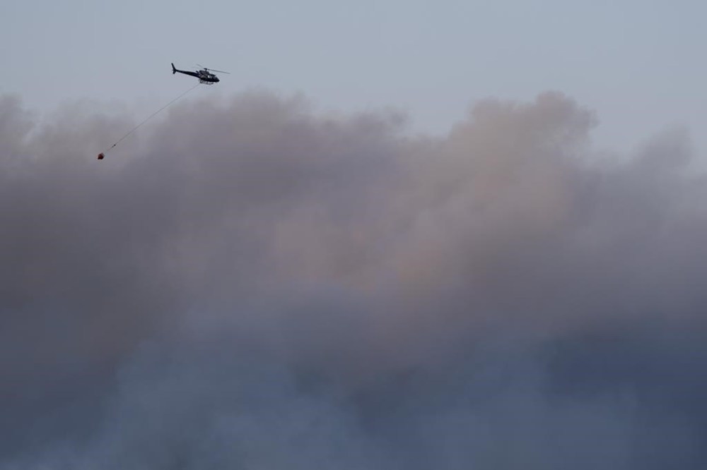A helicopter carrying water flies through heavy smoke as an out-of-control wildfire in a suburban community outside of Halifax quickly spread, engulfing multiple homes and forcing the evacuation of local residents on May 28.THE CANADIAN PRESS/Darren Calabrese