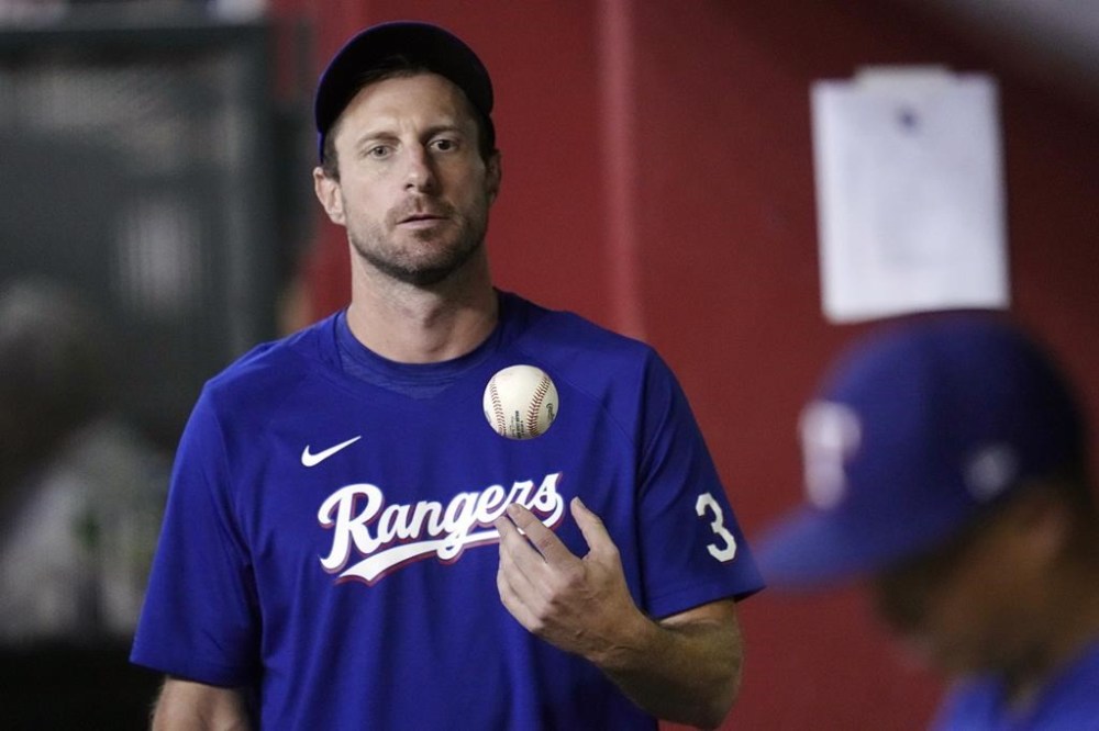 FILE- Texas Rangers' Max Scherzer flips the ball in the air as he paces the dugout during the seventh inning of a baseball game against the Arizona Diamondbacks Tuesday, Aug. 22, 2023, in Phoenix. Scherzer had surgery for a herniated disc in his lower back and will miss the start of next season for the World Series champion Texas Rangers. General manager Chris Young said Friday, Dec. 15, 2023, that Scherzer, who was removed from the roster during the World Series because of back discomfort, had surgery Thursday, Dec. 14, after injections and other less-evasive treatments didn't relieve the pain. (AP Photo/Ross D. Franklin, File)