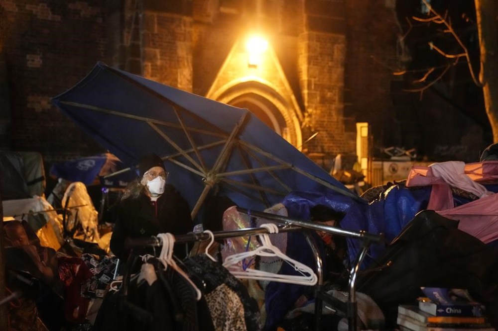 Rev. Canon Maggie Helwig stands guard over a remaining encampment resident (obscured) at the tented community outside of the St. Stephen-In-The-Fields Anglican Church in Toronto on Friday Nov. 24, 2023, as the City of Toronto begins to clear out an encampment in Kensington Market. THE CANADIAN PRESS/Chris Young