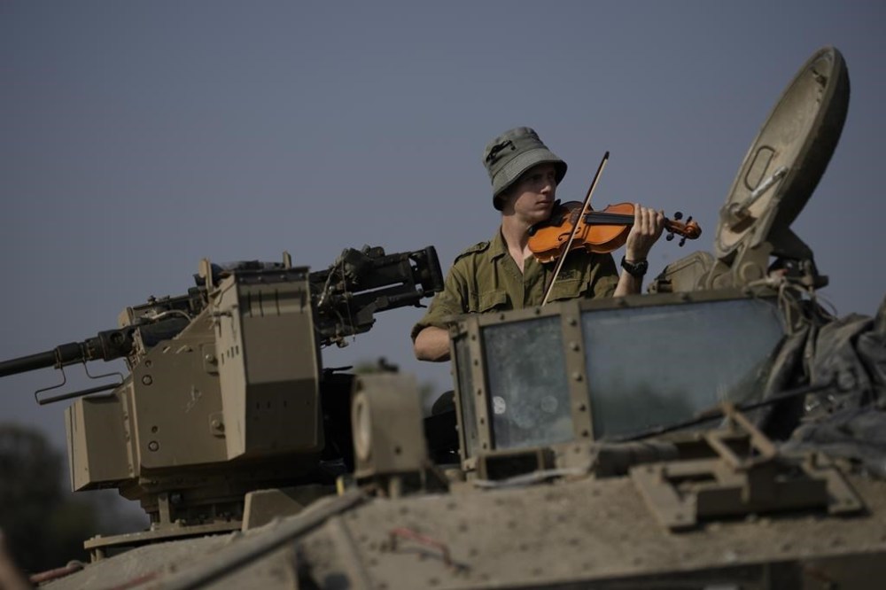 An Israeli soldier plays a violin in an armored vehicle near the border of the Gaza Strip, Monday, Dec. 18, 2023. (AP Photo/Leo Correa)