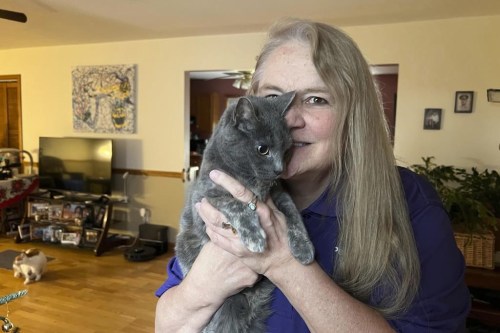 Juanita Mengel holds her cat Lola-Pearl in her home in Amanda, Ohio on Monday, Dec. 11, 2023. More than five years ago, someone left the kitten with twisted back legs at a Missouri animal shelter. The cat was transferred to specialists in Iowa who amputated her left hind leg. She was soon after adopted by Mengel who lost her left leg after a near-fatal car accident. Now the duo has partnered with a nonprofit that registers therapy animal volunteer teams. They visit hospitals, nursing homes and even amputee support groups to aid in therapy and other activities to improve well-being in communities. (AP Photo/Patrick Orsagos)