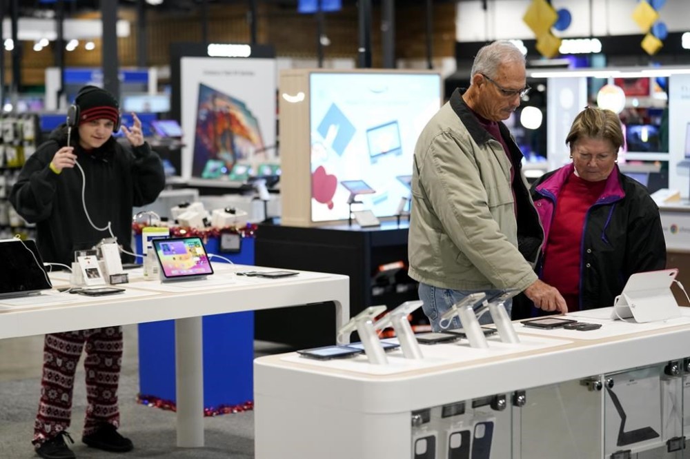 FILE - Bob Adkison, center, and his wife Rosie, right, browse computer tablets at a Best Buy store, Friday, Nov. 24, 2023, in Charlotte, N.C. Preparing for a midnight toast and more year-end festivities may require a run or two to the store — but you’ll want to prepare for some limited business hours.(AP Photo/Erik Verduzco, File)