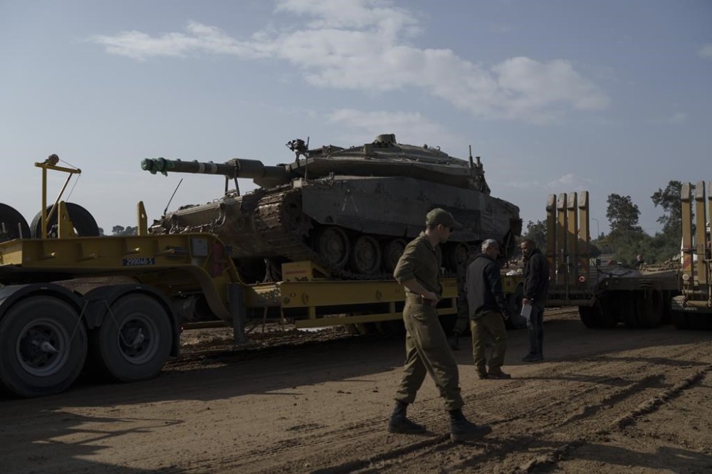 Israeli soldiers load a tank on a transport truck in a staging area at the Israeli-Gaza border in southern Israel, Tuesday, Jan. 2, 2024. The army said Monday that several thousand troops would be taken out of Gaza in the coming weeks. Some will head to bases for further training or rest, while many older reservists will go home. (AP Photo/Leo Correa)