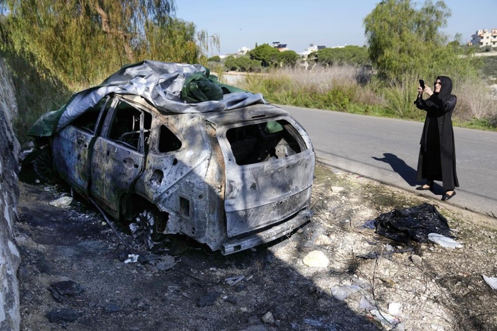 A woman takes pictures of a burned and damaged car that was used by the senior Hezbollah commander Wissam Tawil, who was killed on Monday, in Kherbet Selem village, south Lebanon, Tuesday, Jan. 9, 2024. An Israeli airstrike killed Tawil, who is an elite Hezbollah commander in southern Lebanon, the latest in an escalating exchange of strikes along the border that have raised fears of another Mideast war even as the fighting in Gaza exacts a mounting toll on civilians. (AP Photo/Hussein Malla)