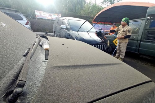 A disaster management agency official washes a car covered in volcanic ash from the eruption of Mount Marapi in Agam, West Sumatra, Indonesia, Sunday, Jan. 14, 2024. Dozens of people living on the slopes of Mount Marapi have been evacuated from their homes after Indonesian authorities raised the alert level of of the nearly 2,900-meter (9,480-foot) volcano to the second highest as it continues to erupt. (AP Photo/Givo Alputra)