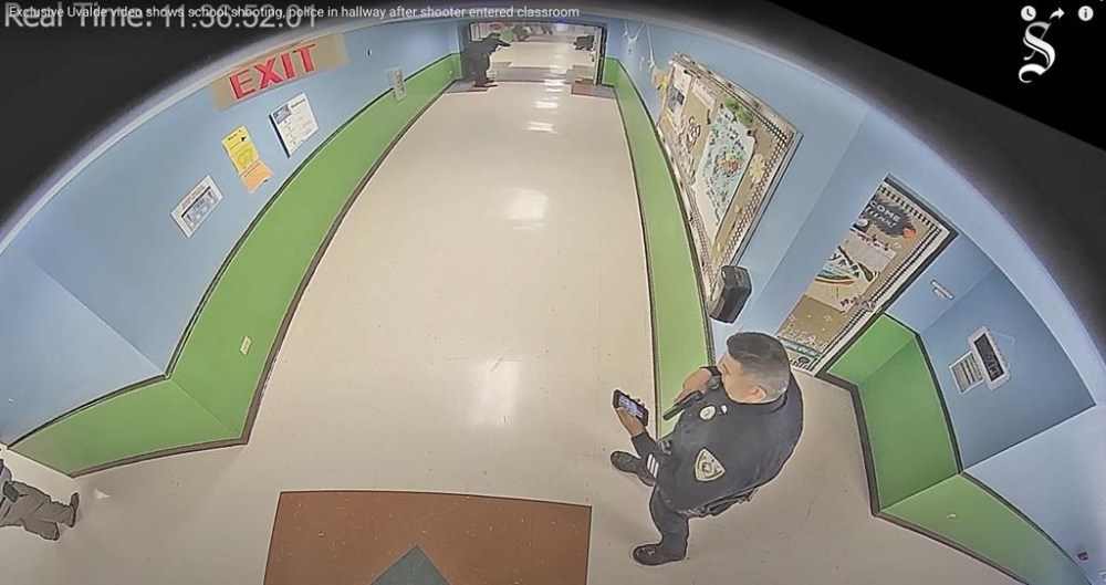 FILE - In this photo taken from surveillance video provided by the Uvalde Consolidated Independent School District via the Austin American-Statesman, shows officer Ruben Ruiz, whose wife, Eva Mireles was killed in the shooting, checking his phone in the hallway at Robb Elementary School in Uvalde, Texas, May 24, 2022. A Justice Department report released Thursday, Jan. 18, 2024 details a myriad of failures by police who responded to the Uvalde, Texas school shooting that led to children waiting desperately for over an hour before officers stormed a classroom to take down the gunman. (Uvalde Consolidated Independent School District/Austin American-Statesman via AP, file)