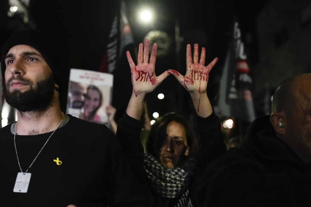 Relatives and supporters of the Israeli hostages held in the Gaza Strip by the Hamas militant group attend a protest calling for their release outside the Knesset, Israel's parliament, in Jerusalem, Monday, Jan. 22, 2024. Hebrew on the hands with fake blood reads,