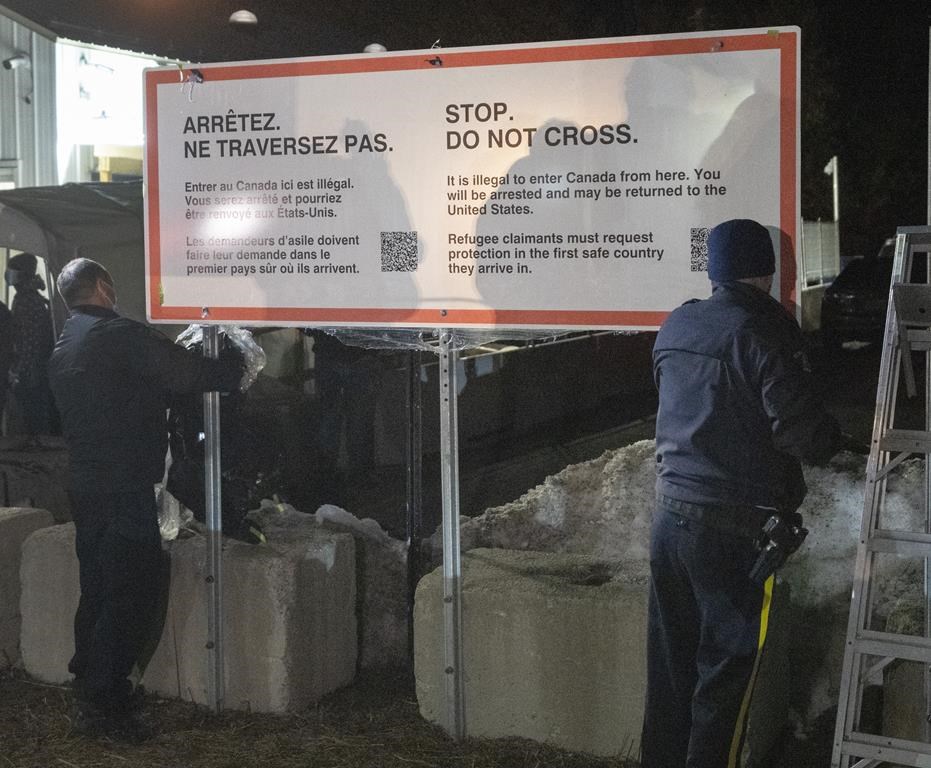 RCMP officers unwrap a new warning sign for asylum seekers on the border at Roxham Road from New York into Canada Saturday March 25, 2023, in Champlain, N.Y. RCMP have charged two Montreal men with conspiracy after they were allegedly caught trying to smuggle people across the border into the United States last year. THE CANADIAN PRESS/Ryan Remiorz