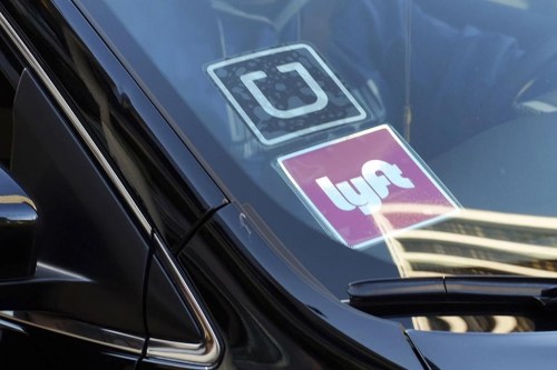 FILE - In this Jan. 12, 2016, file photo, a ride share car displays Lyft and Uber stickers on its front windshield in downtown Los Angeles. Thousands of U.S. ride-hailing workers plan to park their cars and picket at major U.S. airports Wednesday, Feb. 14, 2024, in what organizers say is their largest strike yet in a drive for better pay and benefits. (AP Photo/Richard Vogel, File)