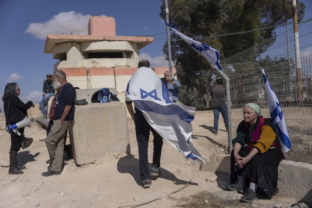 People stand in front of a gate at the Nitzana border crossing with Egypt, in southern Israel, Wednesday, Feb. 14, 2024, protesting against the humanitarian aid to enter Gaza until all the hostages are released. (AP Photo/Ohad Zwigenberg)