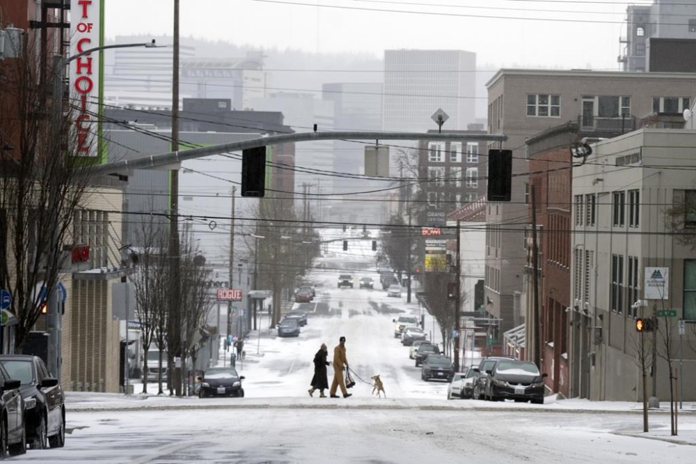 A person walks a dog as they cross SE Belmont Street in the snow on Saturday, Jan. 13, 2024, in Portland, Ore. Officials in Oregon's Multnomah County, home to Portland, say they will declare a state of emergency Wednesday evening due to potential snow. The National Weather Service says up to three inches of snow could fall Wednesday, Feb. 13, through Thursday afternoon. (AP Photo/Jenny Kane)