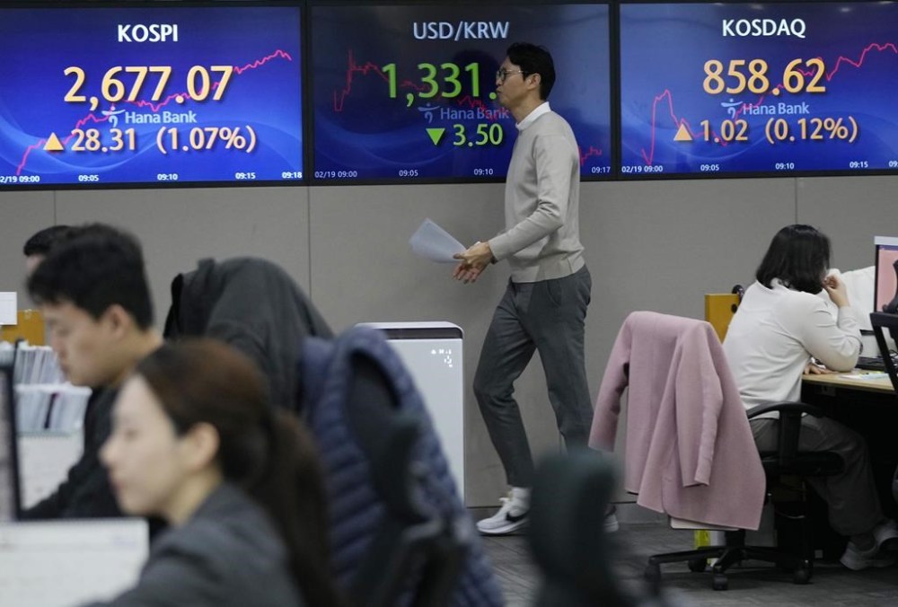 A currency trader passes by the screens showing the Korea Composite Stock Price Index (KOSPI), left, and the foreign exchange rate between U.S. dollar and South Korean won, center, at the foreign exchange dealing room of the KEB Hana Bank headquarters in Seoul, South Korea, Monday, Feb. 19, 2024. (AP Photo/Ahn Young-joon)