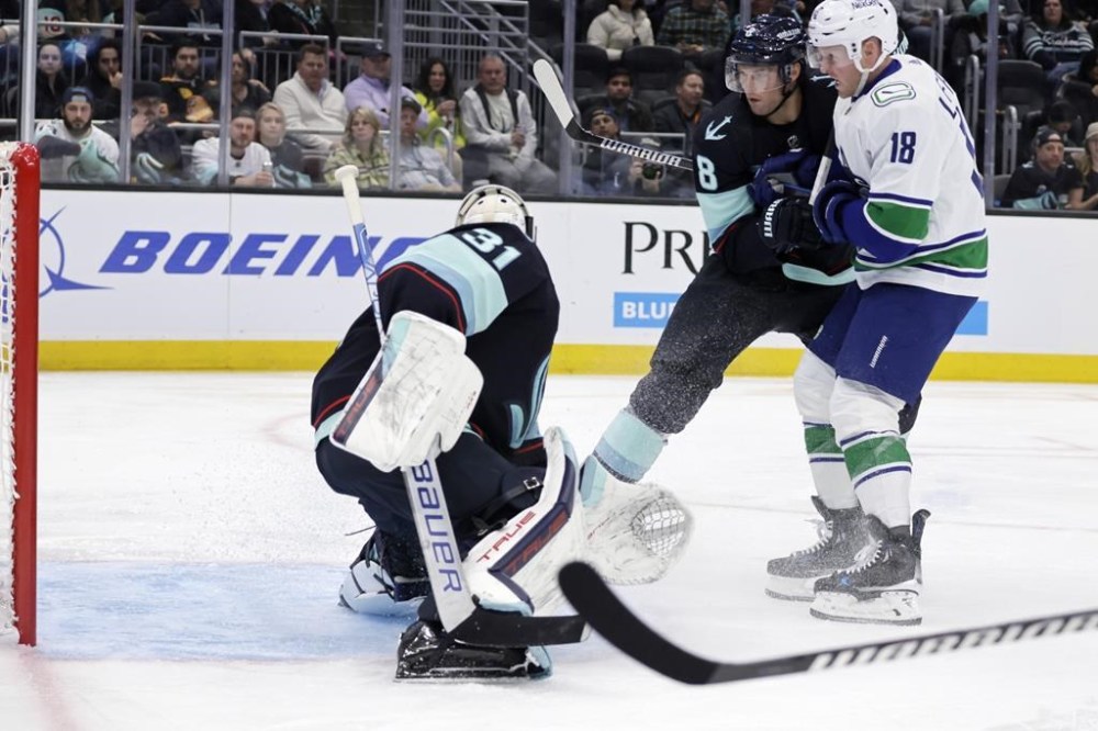 Vancouver Canucks center Sam Lafferty (18) watches his shot in the goal past Seattle Kraken goaltender Philipp Grubauer with defenseman Brian Dumoulin (8) defending during the second period of an NHL hockey game, Thursday, Feb. 22, 2024, in Seattle. (AP Photo/John Froschauer)