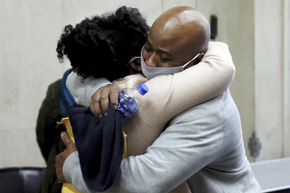 FILE - James Lucien, right, is embraced Tuesday, Dec. 7, 2021, by a family member, left, at Suffolk Superior Court in Boston, after being freed from incarceration. Lucien, who spent more than two decades in prison for a murder conviction that was thrown out by the courts is suing the state for $1 million. Lucien was serving a life sentence in connection to a 1994 fatal shooting when he was released in 2021. (Jessica Rinaldi/The Boston Globe via AP, File)
