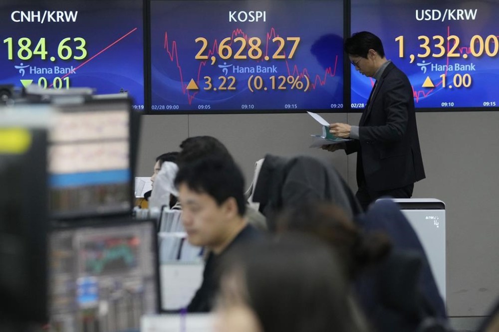 A currency trader moves past the screens showing the Korea Composite Stock Price Index (KOSPI), center, and the foreign exchange rate between U.S. dollar and South Korean won, right, at the foreign exchange dealing room of the KEB Hana Bank headquarters in Seoul, South Korea, Wednesday, Feb. 28, 2024. Asian markets were mostly lower on Wednesday after U.S. stocks held near their record levels in a quiet day of trading. (AP Photo/Ahn Young-joon)
