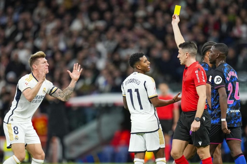 Referee Isidro Díaz de Mera shows a yellow card to Real Madrid's Toni Kroos, left, during a Spanish La Liga soccer match between Real Madrid and Sevilla at the Santiago Bernabeu stadium in Madrid, Spain, Sunday, Feb. 25, 2024. (AP Photo/Manu Fernandez)
