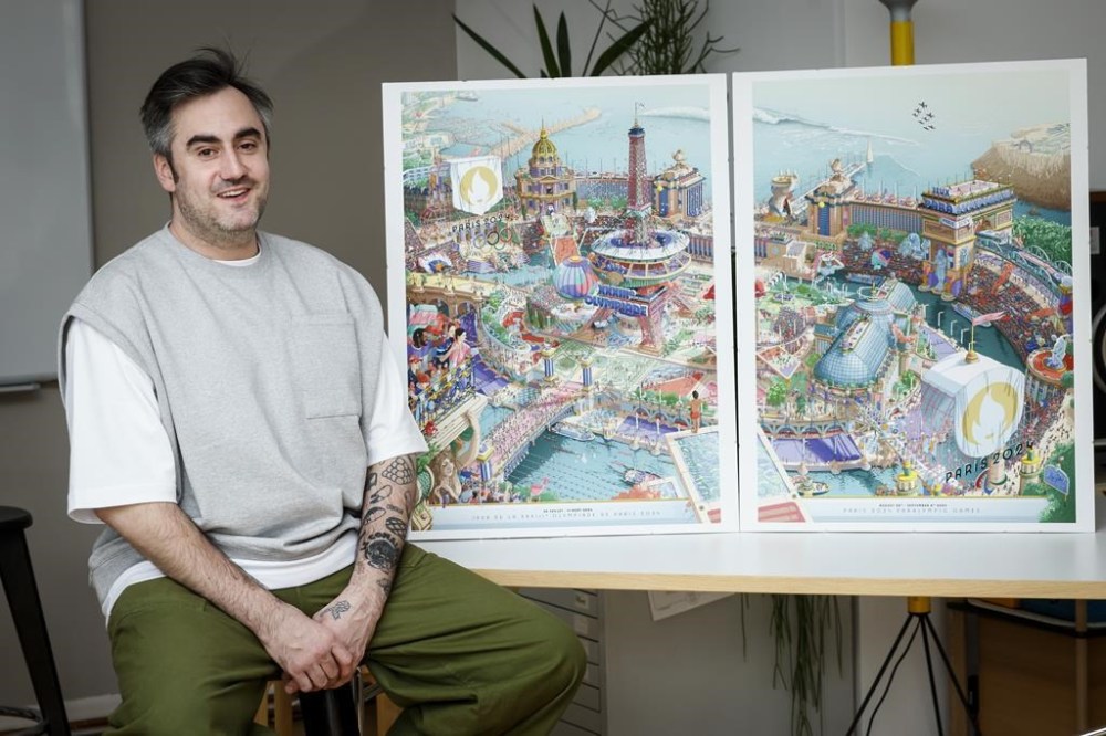 French artist Hugo Gattoni poses next to the Paris 2024 Olympic and Paralympic posters at his workshop, in Ivry-sur-Seine, outside Paris, Tuesday Feb. 20, 2024. Vibrant colors and striking landmarks illuminate posters for the Paris Olympic Games in an Art Deco style inspired by the city's flamboyant past. The posters have been unveiled at the Musée d'Orsay. (AP Photo/Thomas Padilla)