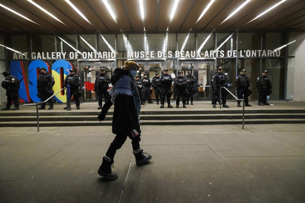 A protester walks as police line the entrance to the Art Gallery of Ontario, where a cancelled event for Canada's Prime Minister Justin Trudeau and Italy's Prime Minister Giorgia Meloni, was to take place, in Toronto, Saturday, Mar. 2, 2024. THE CANADIAN PRESS/Cole Burston