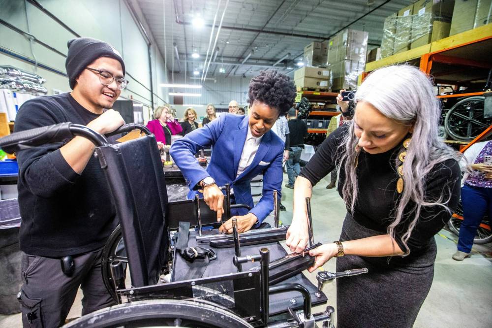 MIKAELA MACKENZIE / FREE PRESS
Field technician Norman Moreno (left) shows health minister Uzoma Asagwara and families minister Nahanni Fontaine the basics of wheelchair repair at Manitoba Possible in Winnipeg on Friday. The province announced funding for two more technicians at the Manitoba Wheelchair Program, which it hopes will cut wait times for clients.