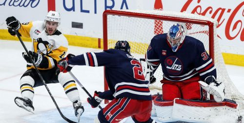 Winnipeg Jets goaltender Connor Hellebuyck (37) saves the shot as Pittsburgh Penguins' Reilly Smith (19) stumbles and Dylan DeMelo (2) defends during third period NHL action in Winnipeg on Saturday, February 10, 2024. THE CANADIAN PRESS/John Woods