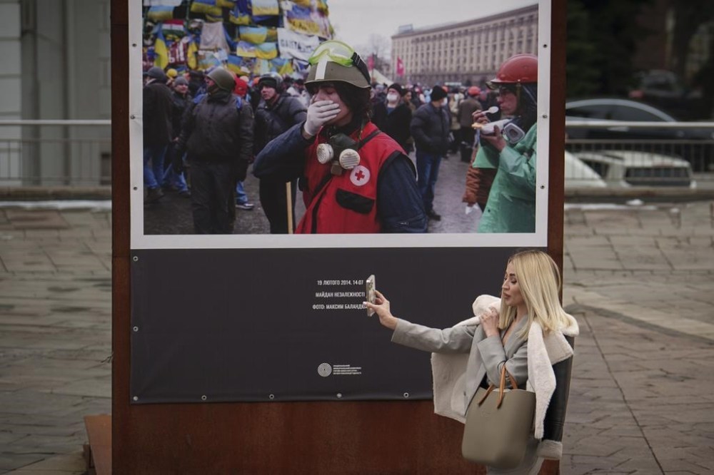 A woman walks holding her mobile phone past a photograph showing a scene from the 2014 Maidan revolution in Kyiv, Ukraine, Thursday, March 14, 2024. Ukraine fired at least eight missiles at Russia's Belgorod border region, killing one person and wounding six, local officials said Thursday, as Kyiv's forces apparently kept up their efforts to rattle the Kremlin on the eve of Russia's presidential election, a vote that is taking place amid a ruthless crackdown on dissent. (AP Photo/Vadim Ghirda)