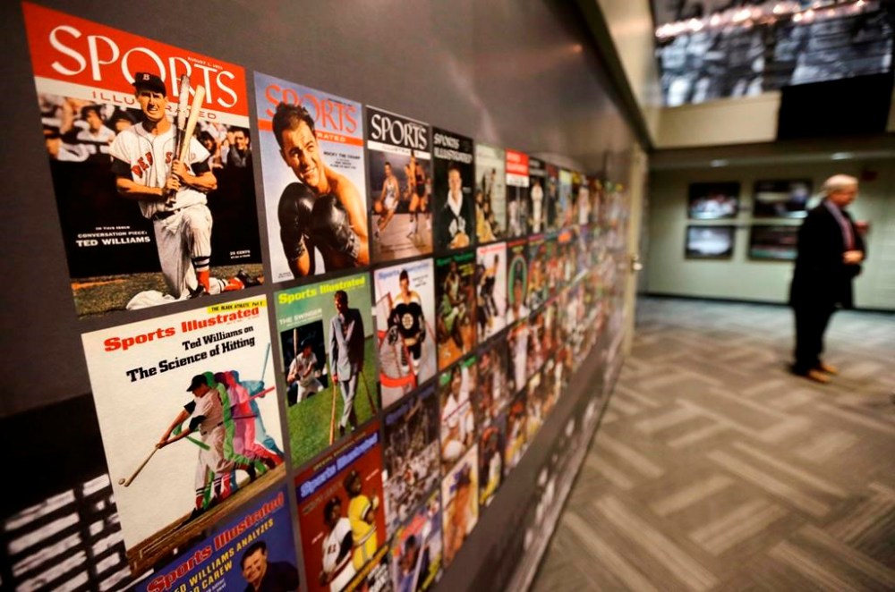 FILE - The Sports Museum curator Richard Johnson, right, stands near an exhibit that displays cover photos from the sports magazine Sports Illustrated in the museum at the TD Garden, in Boston, Dec. 17, 2015. Sports Illustrated will continue operations after the company that owns the brand reached an agreement with a new publisher for its print and digital products, Monday, March 18, 2024. (AP Photo/Steven Senne, File)