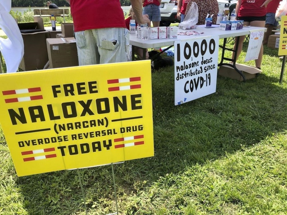 FILE - Signs are displayed at a tent during a health event, June 26, 2021, in Charleston, W.Va. Naloxone is a drug that reverses the effects of an opioid overdose by helping the person breathe again. A federal appeals court asked West Virginia’s highest court Monday, March 18, 2024, to address what constitutes a public nuisance as it reviews a landmark lawsuit against three major U.S. drug distributors. (AP Photo/John Raby, File)