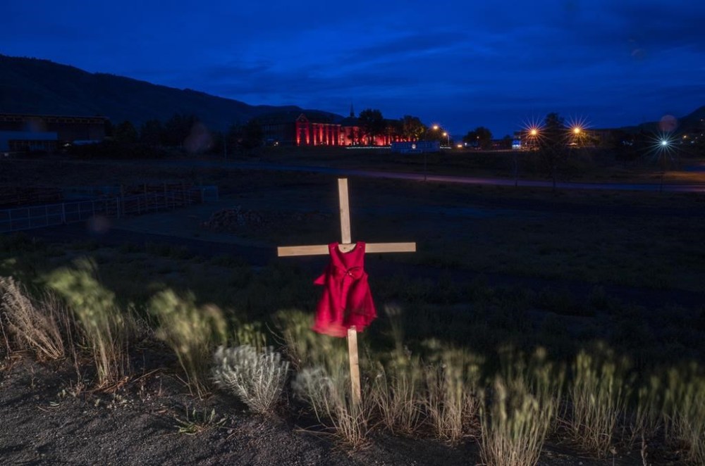 A child's dress is seen on a cross outside a former residential school in Kamloops, B.C., Sunday, June 13, 2021. An interim report from an international group hired to provide advice on identifying and locating the unmarked graves of children who attended residential schools says Canada can should continue funding searches beyond 2025. THE CANADIAN PRESS/Jonathan Hayward