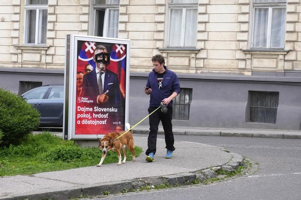 A man walks his dog past a poster for Peter Pellegrini, who currently serves as Parliament's speaker, one of the nine candidates in the upcoming Slovakia's presidential election, Bratislava, Slovakia, Friday, March 22, 2024. (AP Photo/Petr David Josek)