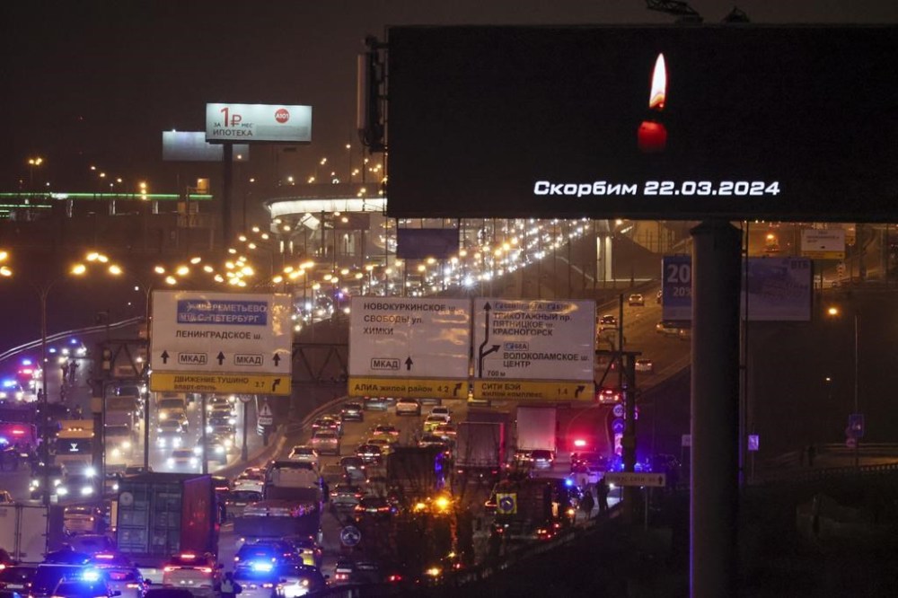 Traffic on the highway is visible near the Crocus City Hall with a warning message on a billboard that reads