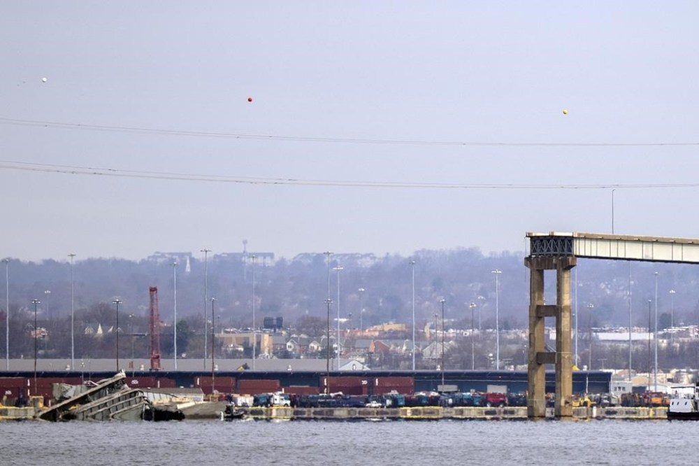 A collapsed span of the Francis Scott Key Bridge sits in the water on Tuesday, March 26, 2024, as seen from Pasadena, Md. A container ship rammed into a major bridge in Baltimore early Tuesday, causing it to collapse in a matter of seconds and creating a terrifying scene as several vehicles plunged into the chilly river below. (AP Photo/Mark Schiefelbein)