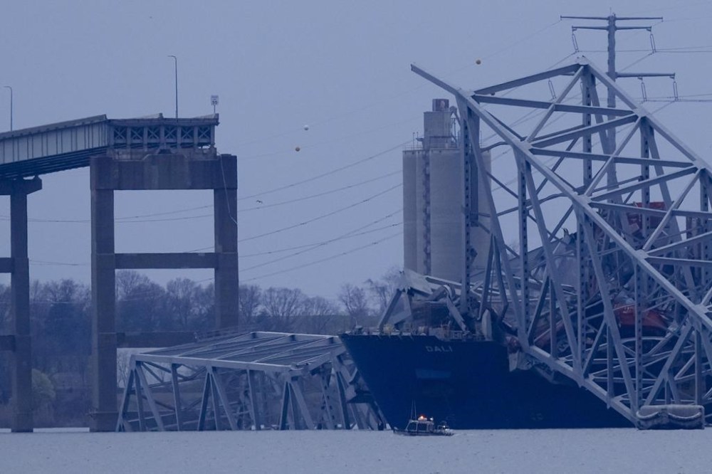 A container ship rests against wreckage of the Francis Scott Key Bridge as night falls on Tuesday, March 26, 2024, as seen from Sparrows Point, Md. The ship rammed into the major bridge in Baltimore early Tuesday, causing it to collapse in a matter of seconds and creating a terrifying scene as several vehicles plunged into the chilly river below. (AP Photo/Matt Rourke)