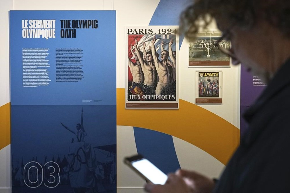 A man checks his phone during an exhibition press day, Wednesday, March 27, 2024 in Paris. Ahead of this summer's Paris Olympics, an exhibit in the French capital shows how the Games have been a