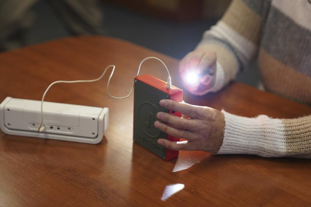 Minh Ha, assistive technology manager at the Perkins School for the Blind uses a flashlight to try a LightSound device, attached to an external speaker, for the first time at the school's library in Watertown, Mass., on March 2, 2024. Wanda Díaz-Merced, an astronomer who is blind, a co-creator of the device, says, “The sky belongs to everyone. And if this event is available to the rest of the world, it has to be available for the blind, too. ... I want students to be able to hear the eclipse, to hear the stars.