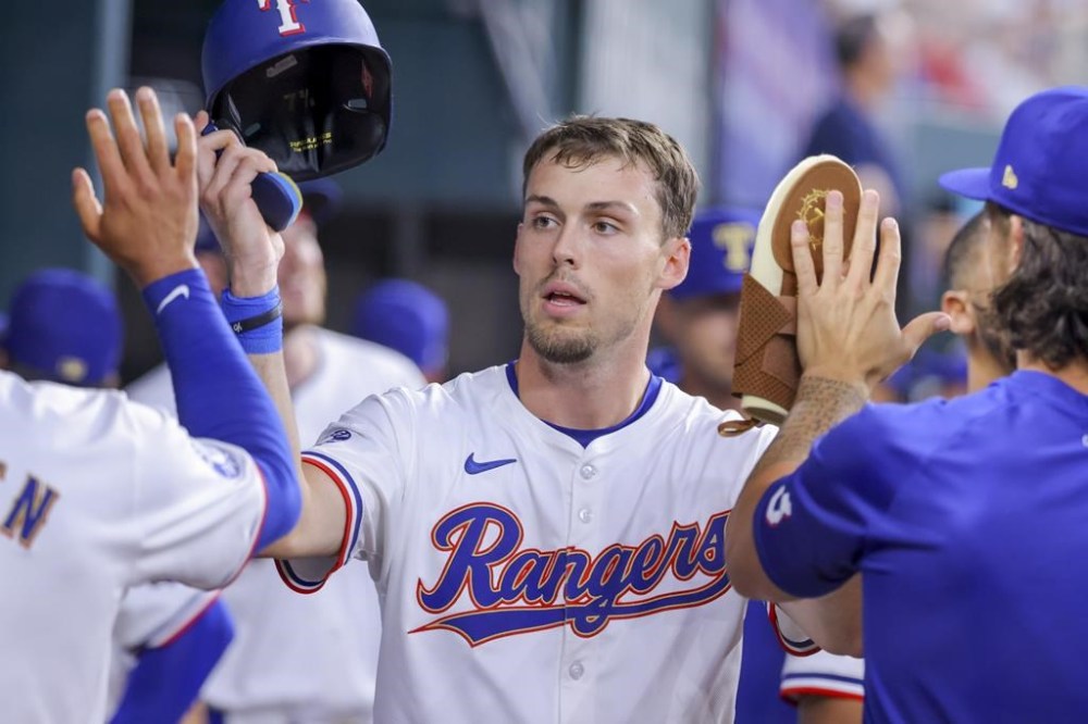 Texas Rangers' Evan Carter celebrates in the dugout after scoring on a two-run triple from Wyatt Langford during the fourth inning of a baseball game against the Chicago Cubs, Sunday, March 31, 2024, in Arlington, Texas. (AP Photo/Gareth Patterson)