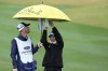 Lydia Ko, right, with her caddie, tries to keep dry at the third green during the final round of LPGA Ford Championship golf tournament Sunday, March 31, 2024, in Gilbert, Ariz. (AP Photo/Ross D. Franklin)