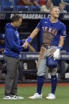 A Texas Rangers trainer, left, looks over Josh Jung after he was hit by a foul ball against the Tampa Bay Rays during the ninth inning of a baseball game Monday, April 1, 2024, in St. Petersburg, Fla. Jung left the game and was replaced by a pinch hitter. (AP Photo/Steve Nesius)