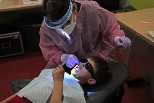 Clayton Warner holds a mirror as dental hygienist Mary Davis examines his teeth at the Christa McAuliffe School in Concord, N.H., Wednesday, Feb. 21, 2024. (AP Photo/Robert F. Bukaty)