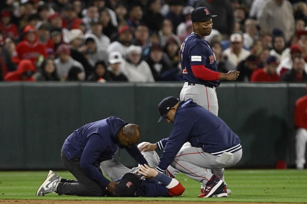 Boston Red Sox shortstop Trevor Story receives attention from a trainer and manager Alex Cora, right, after being injured on a single by Los Angeles Angels' Mike Trout during the fourth inning of a baseball game in Anaheim, Calif., Friday, April 5, 2024. (AP Photo/Alex Gallardo)