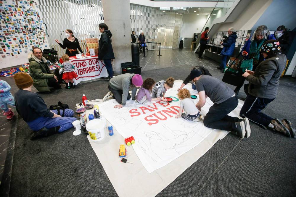 Supporters of keeping the Millennium Library open on Sundays work on a sign at the downtown library Sunday. (John Woods / Free Press)