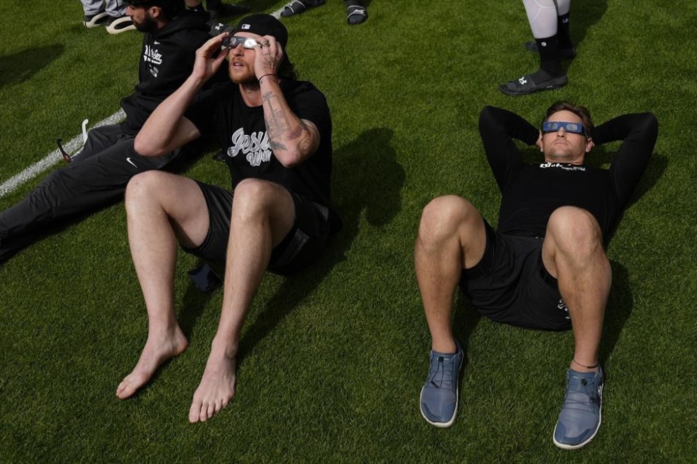 Chicago White Sox pitchers Tanner Banks, right, and Michael Kopech, left, look up through eclipse safely glasses from the glass outside the dugout as the moon partially covers the sun during a total solar eclipse, at Progressive Field in Cleveland, on Monday, April 8, 2024, before the Cleveland Guardians home opener Baseball game against the Chicago White Sox. (AP Photo/Carolyn Kaster)