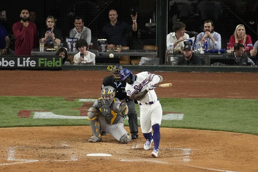Texas Rangers' Adolis Garcia follows through on a two-run single as Oakland Athletics' Shea Langeliers and umpire Ramon De Jesus look on in the fourth inning of a baseball game in Arlington, Texas, Wednesday, April 10, 2024. The hit scored Corey Seager and Marcus Semien. (AP Photo/Tony Gutierrez)