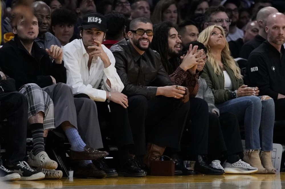 Bad Bunny, center, watches the second half of an NBA basketball game between the Golden State Warriors and the Los Angeles Lakers in Los Angeles, Saturday, March 16, 2024. (AP Photo/Ashley Landis)