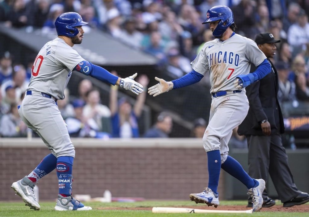 Chicago Cubs' Dansby Swanson, right, is congratulated by Mike Tauchman, left, after scoring during the second inning of a baseball game against the Seattle Mariners, Saturday, April 13, 2024, in Seattle. (AP Photo/Stephen Brashear)