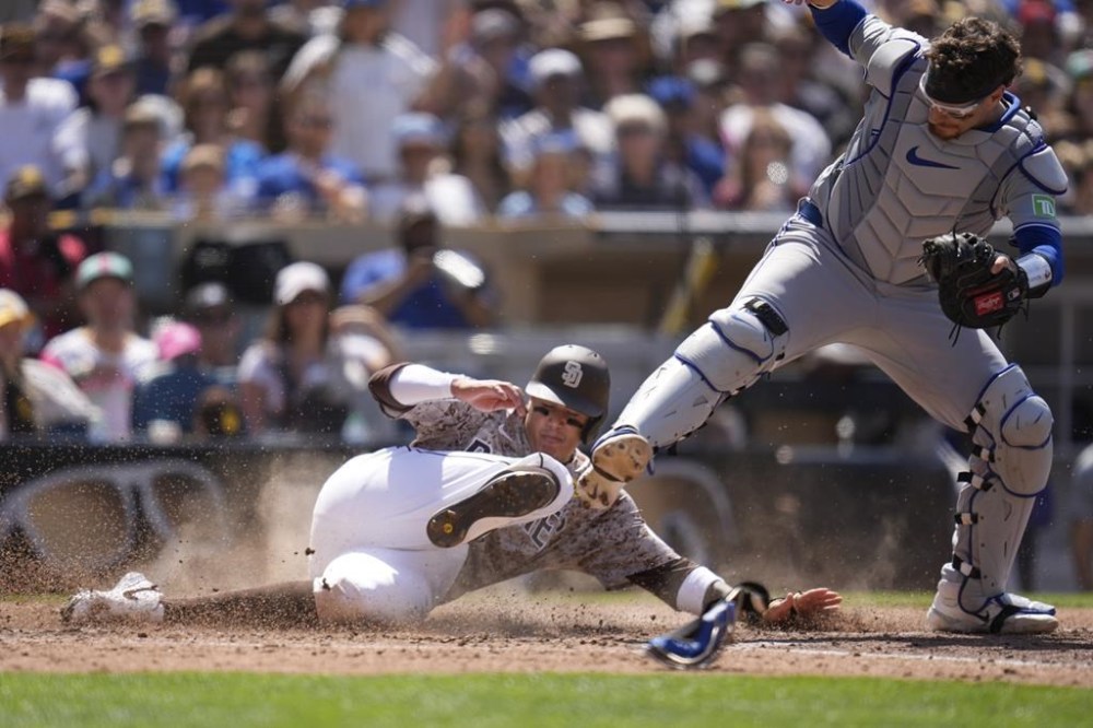 San Diego Padres' Manny Machado, left, slides in late to home after Jackson Merrill grounded into a force out as Toronto Blue Jays catcher Danny Jansen is knocked off the base, right, during the sixth inning of a baseball game, Sunday, April 21, 2024, in San Diego. (AP Photo/Gregory Bull)