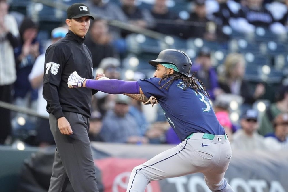 Seattle Mariners' J.P. Crawford, right, celebrates after tripling to drive in three runs as third base umpire Tom Woodring, left, looks on in the second inning of the second game of a baseball doubleheader against the Colorado Rockies, Sunday, April 21, 2024, in Denver. (AP Photo/David Zalubowski)